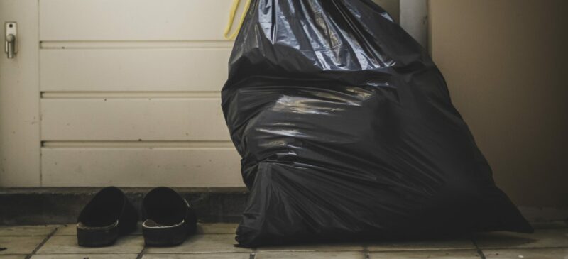 A trash bag next to a pair of shoes in front of the door.